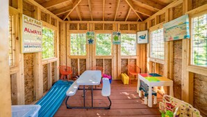 A play area with a slide, tables, and chairs, wooden walls, and windows.