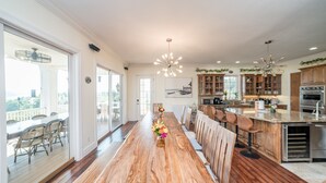 A spacious kitchen with a long wooden table, bar stools, and a view of the outdoors.