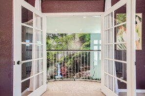 Een deuropening naar een balkon met uitzicht op een waterval en groen.