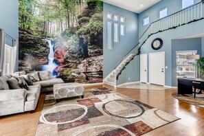 Een ruime woonkamer met een groot muurschildering van een waterval, een trap en een zithoek met een salontafel.