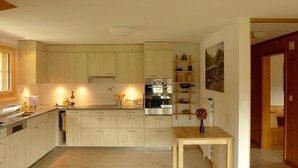 Una cocina moderna con armarios de madera clara, horno empotrado y una mesa de madera con un jarrón.