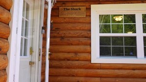 En træhytte med en skilt, der siger "The Shack", og et vindue med udsigt til grøn vegetation.