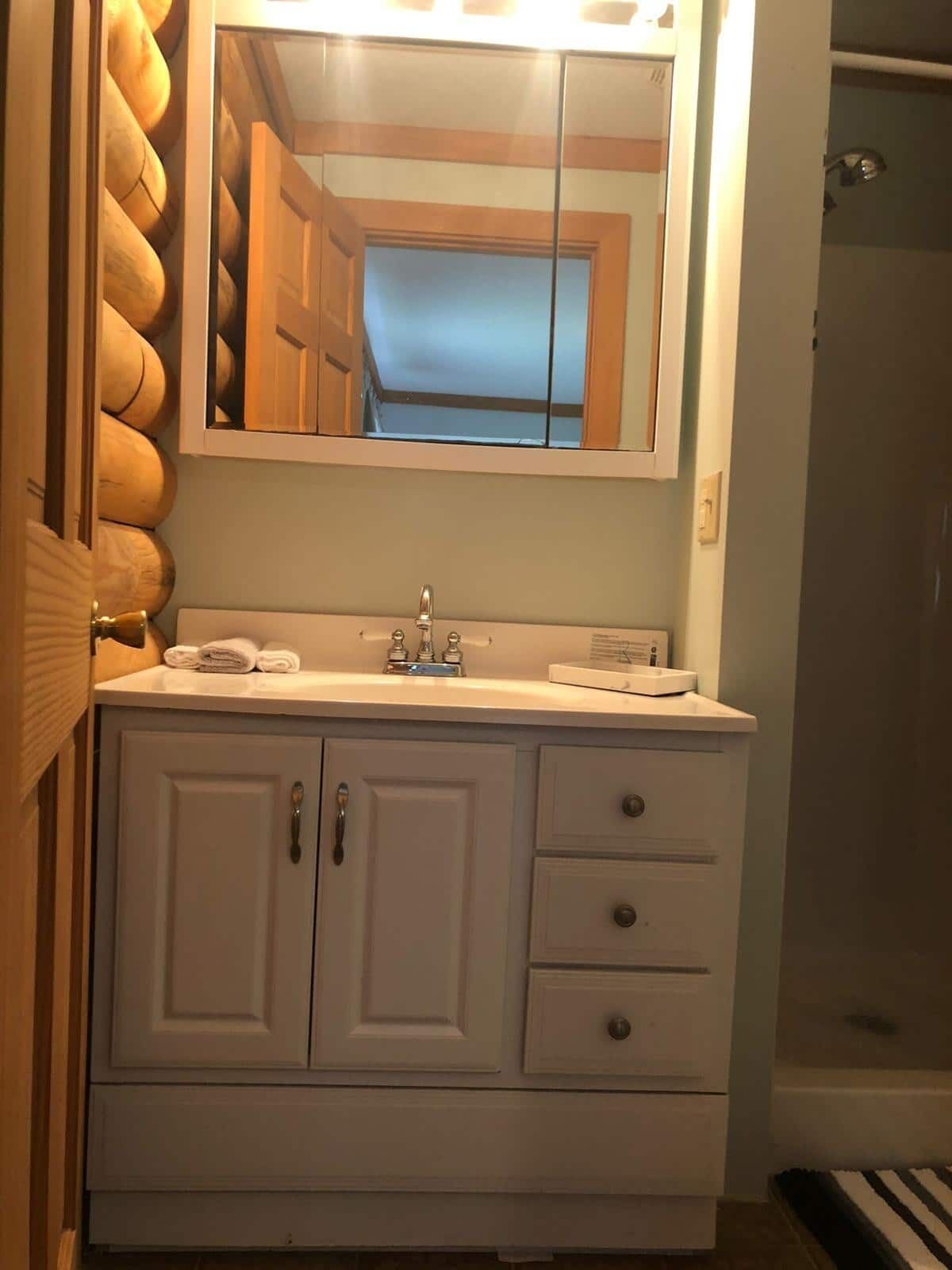 A bathroom with a white vanity, a mirror, and a shower area.