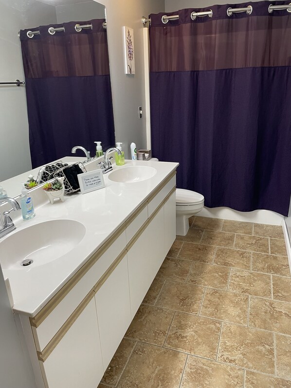 Une salle de bain avec un lavabo blanc, deux miroirs, des toilettes et un rideau de douche.
