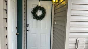 Una puerta blanca con detalles verdes, un felpudo y una corona decorativa.