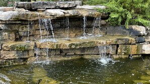 Uma cascata de pedra natural deságua num lago rodeado por rochas e vegetação.
