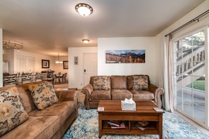 A living room with two brown leather sofas, a wooden coffee table, and a large window with a view of a building. - Walk to Mountain or Steps to Free Bus Stop/HotTub w/Private Garage-W/D in Unit-Gas Fireplace (Steamboat Springs)