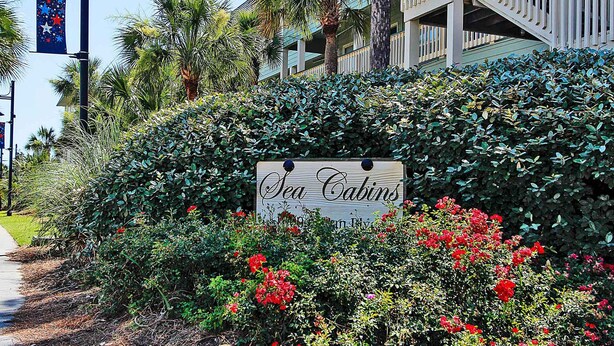 A sign for Sea Cabins on a lush green hedge with red flowers. - Oceanfront, Top Floor/ Corner Sea Cabin, Gorgeous Views with Pool (Isle of Palms)