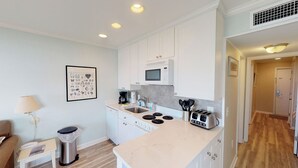 A modern kitchen with white cabinets, a microwave, a sink, and a toaster. There is a framed picture on the wall and a trash can near the seating area. - Oceanfront, Top Floor/ Corner Sea Cabin, Gorgeous Views with Pool (Isle of Palms)
