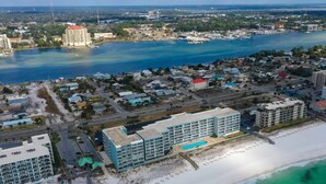 Luftaufnahme einer Küstenstadt mit einem Strandhotel, das über mehrere Etagen verfügt, einem Pool und einem Strandbereich mit Sonnenschirmen.