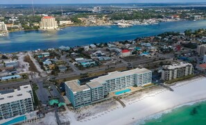 Vista aérea de un pueblo costero con un hotel frente a la playa que tiene varios pisos, una piscina y una zona de playa con sombrillas.