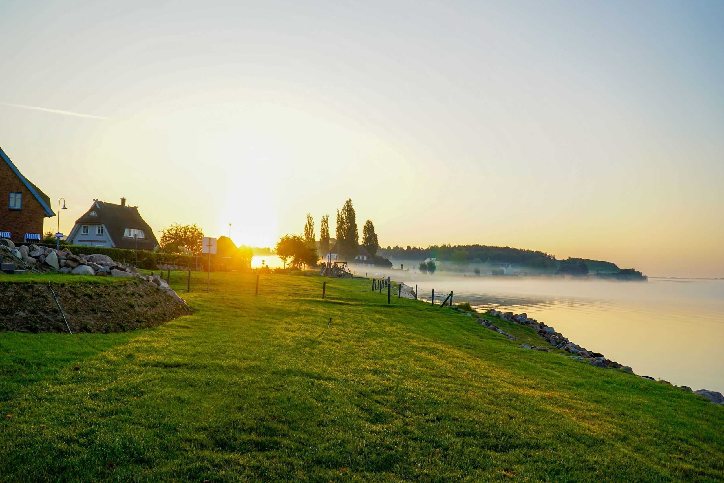 Ruhiger See mit einem Haus und einer Grünfläche im Vordergrund.