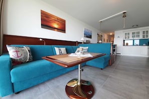 A modern living room with a blue sofa, a wooden coffee table, and a kitchen in the background. - Haus Besch - Apartment Kleine Kapitänskajüte - Kleine Kapitänskajüte: 68m², 2-raum, 2 Pers., Terr., (Mönchgut)