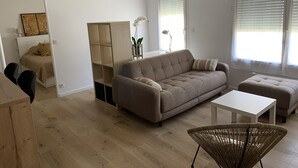 A modern living room with a sofa, ottoman, and a wicker chair. A white table is placed in front of the sofa. - A 20 Mètres des Remparts Appartement Avec Parking (Avignon)