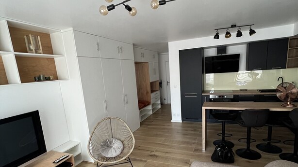 A modern living room with a flat-screen TV, a sofa, a small table, and a fan. There is a kitchen area with a dining table and chairs. - A 20 Mètres des Remparts Appartement Avec Parking (Avignon)