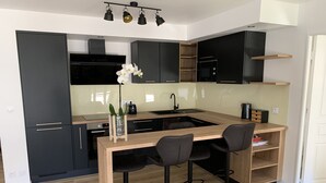 A modern kitchen with a central island, black bar stools, and a small bar area. - A 20 Mètres des Remparts Appartement Avec Parking (Avignon)