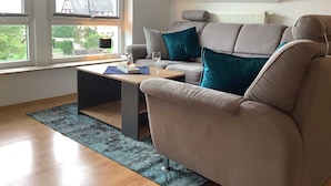 A modern living room with a sofa, a coffee table, and a view of the outdoors through large windows. - Ferienwohnung Pusteblume - 2 Schlafzimmer, Küche, Wohnzimmer, Bad, Balkon (Edertal)