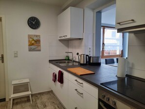 Una cocina moderna con armarios blancos, un lavamanos de acero inoxidable, una tetera, un tostador y una placa de inducción negra.