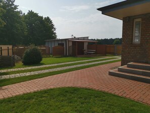 A courtyard with a brick pathway, a small building with a covered area, and a wooden fence.