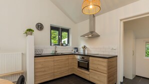 Una cocina moderna con armarios de madera, encimera negra, extractor de acero inoxidable y ventana con vistas a la vegetación.