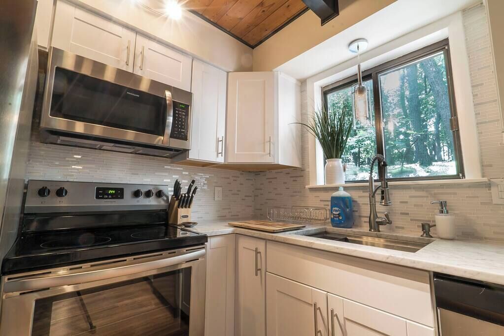 A modern kitchen with stainless steel appliances, white cabinetry, and a large window with a view of trees.