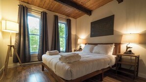 A bedroom with a wooden bed, two bedside tables with lamps, a window with curtains, and a map on the wall.