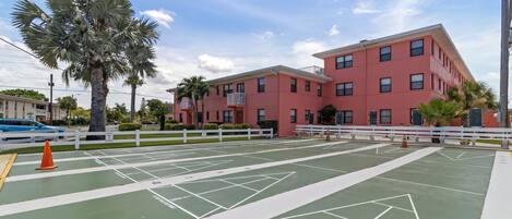 A tennis court with white boundary lines and a palm tree in the foreground.