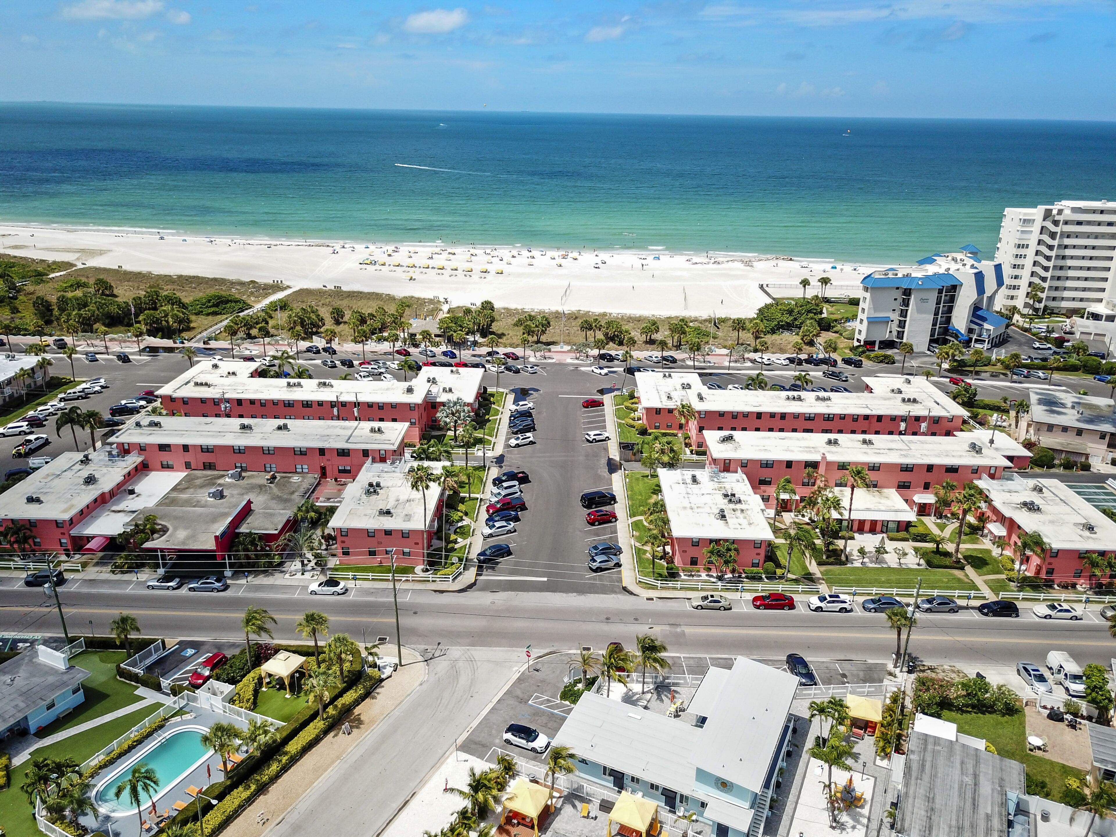 Un hôtel situé en bord de mer, composé de plusieurs bâtiments aux toits rouges, avec un parking et une vue sur l’océan.