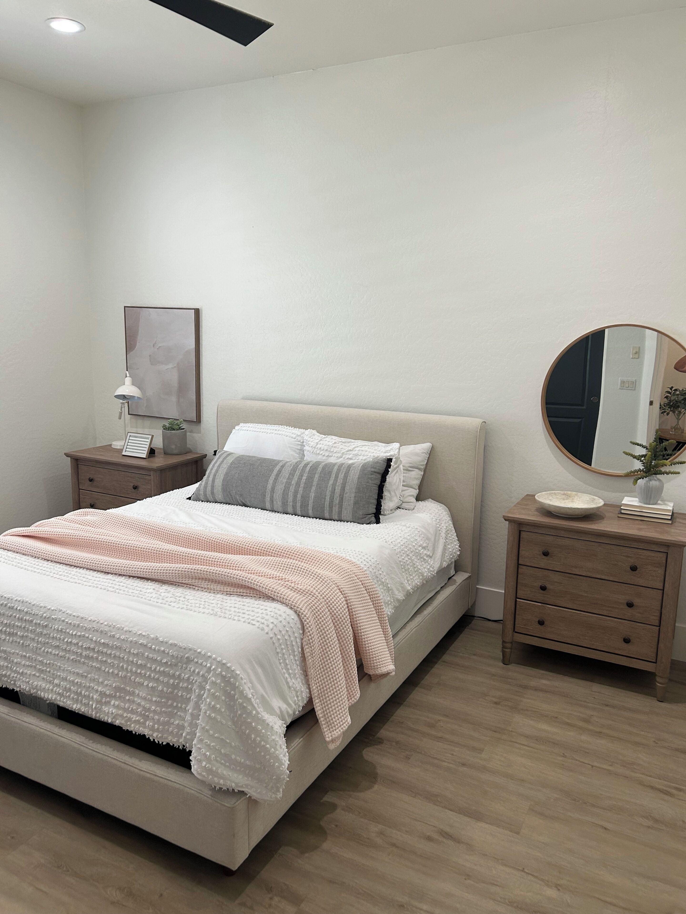 A bedroom with a bed, bedside tables, a mirror, and a wall-mounted picture.