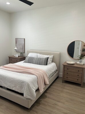 A bedroom with a bed, bedside tables, a mirror, and a wall-mounted picture.