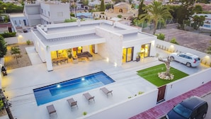 Une maison moderne dotée d’une piscine, d’un espace salon extérieur et d’une voiture garée à proximité.
