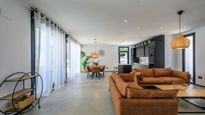 Un salon moderne avec un canapé marron, une table à manger avec des chaises, et un coin cuisine à l’arrière-plan.