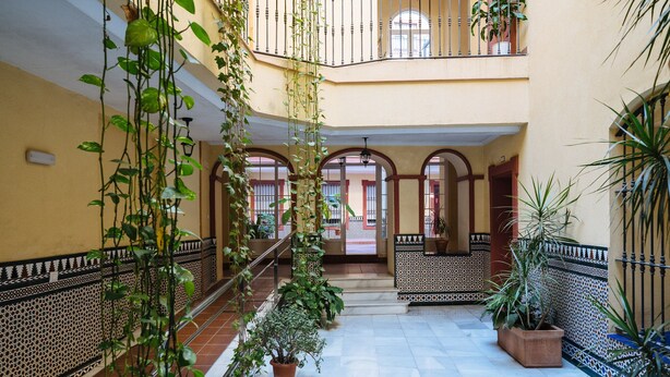 A multi-level atrium with tiled floors, potted plants, and arched doorways. - Beautiful & Bright Apartment for 4 People, Parking Optional (Sevilla)