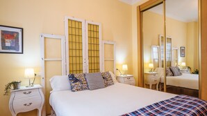A bedroom with a large bed, two bedside tables with lamps, a mirror, and a wall-mounted artwork. - Beautiful & Bright Apartment for 4 People, Parking Optional (Sevilla)