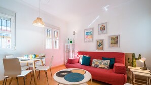 A bright living room with a red sofa, white chairs, a round coffee table, and artwork on the walls. - Beautiful & Bright Apartment for 4 People, Parking Optional (Sevilla)