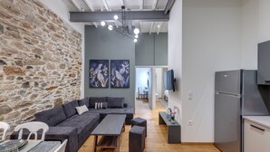 Una sala de estar moderna con pared de piedra, sofá gris y un comedor con mesa y sillas.