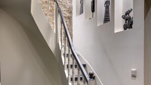 Una escalera con barandillas blancas y escalones grises que conduce a un rellano con un muro de piedra y una puerta.