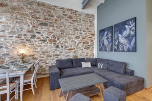 A cozy living area with a stone wall, a grey sectional sofa, a small table, and two wall-mounted paintings.