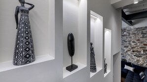 Un interior moderno con diseño minimalista, que presenta una escultura larga de blanco y negro sobre un pedestal, una lámpara de pie negra y elegante, y una pared de piedra con textura.