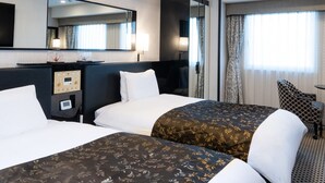Een hotelkamer met twee bedden, een grote spiegel, een bureau met lamp en een raam met gordijnen.