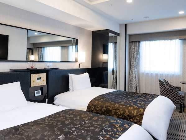 Habitación de hotel con dos camas, un espejo grande, un escritorio con lámpara y una ventana con cortinas.