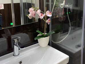 Ein Badezimmer mit einem weißen Waschbecken, einem Spiegel und einer Orchidee im Topf.