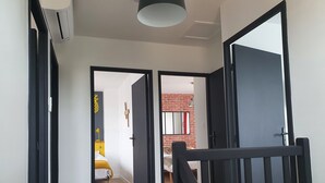 Een gang met een houten vloer die leidt naar een slaapkamer met een bed en een gele lamp.