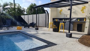 Een zwembadgedeelte met een pergola, zitplaatsen buiten en een bar genaamd 'BAR CITE DES PALMIERS'.