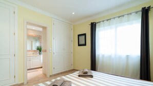 A hotel room with a large bed, a bathroom with a shower, and a view of the outside through a window with curtains. - Outstanding one bedroom apart with heated private pool in Vale do Lobo (Almancil)