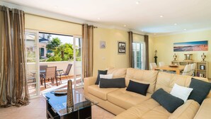 A spacious living room with a large beige sofa, a glass coffee table, and a dining area with a table and chairs. - Outstanding one bedroom apart with heated private pool in Vale do Lobo (Almancil)