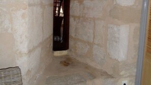 Habitación con paredes de piedra, un pequeño ventanal de arco y un enchufe a la vista.