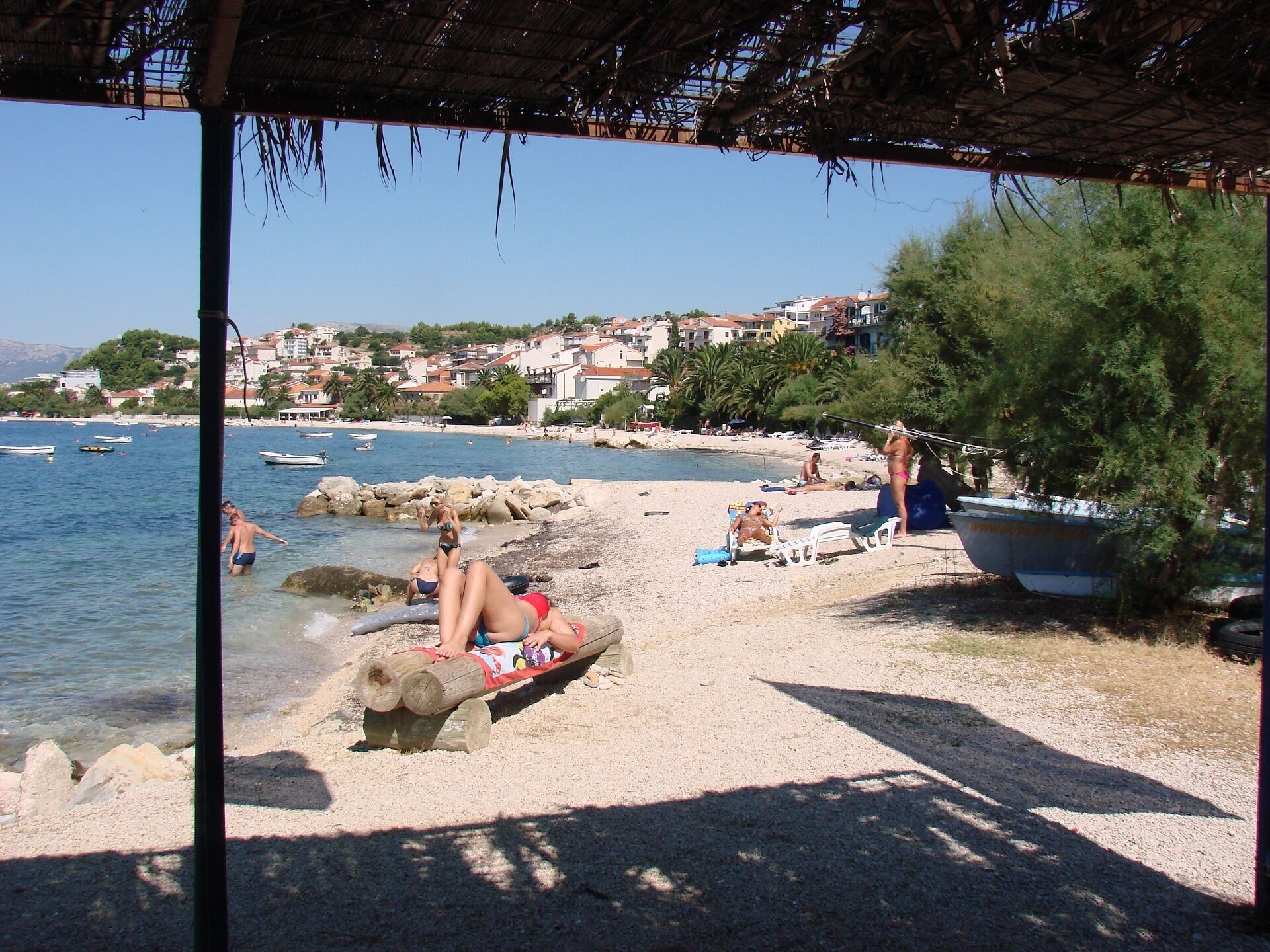 A beach scene with clear skies, a sandy shore, and a few boats in the water.
