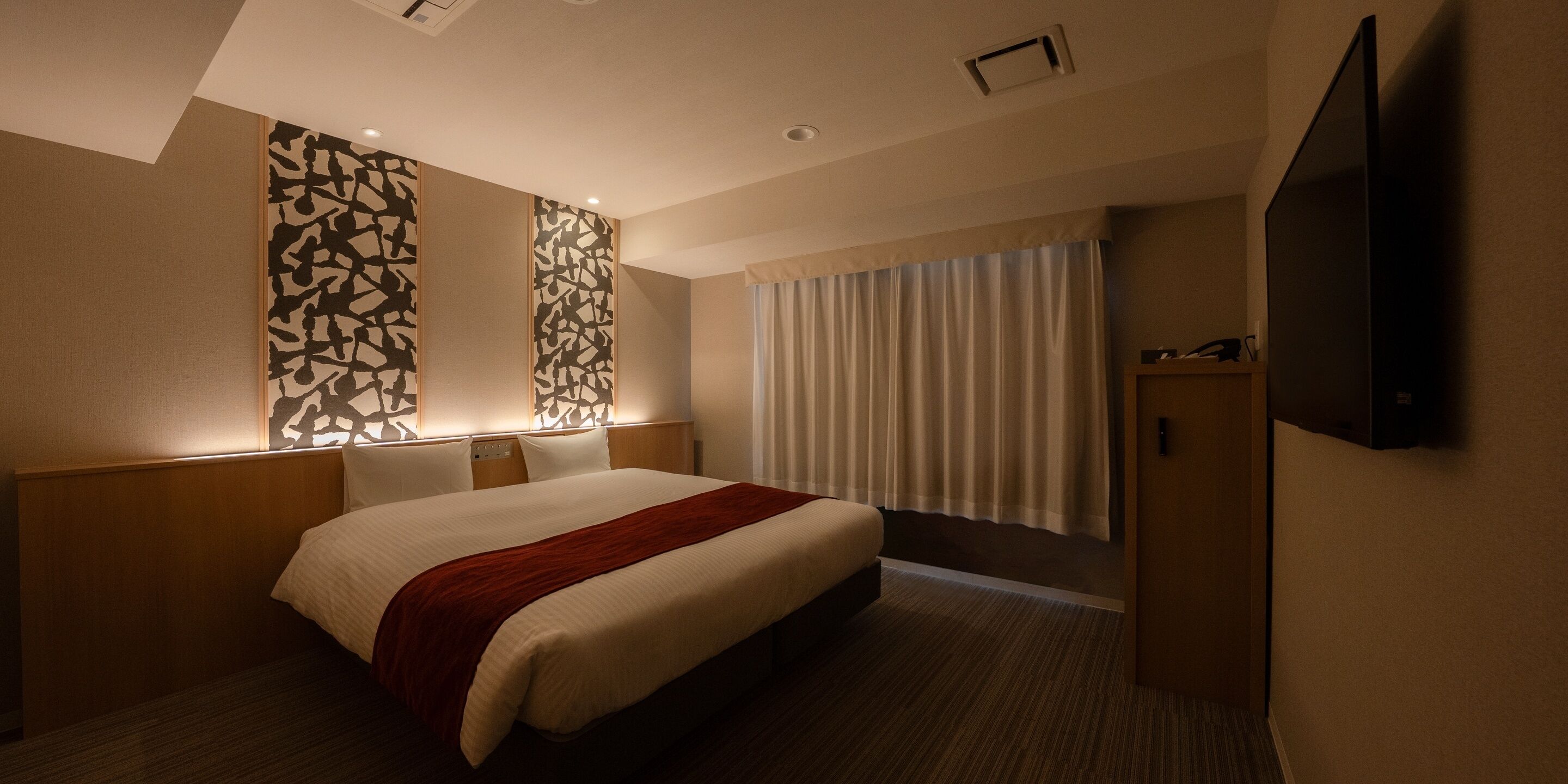 A hotel room with a large bed, a wooden headboard, a flat-screen TV, and a window with curtains.