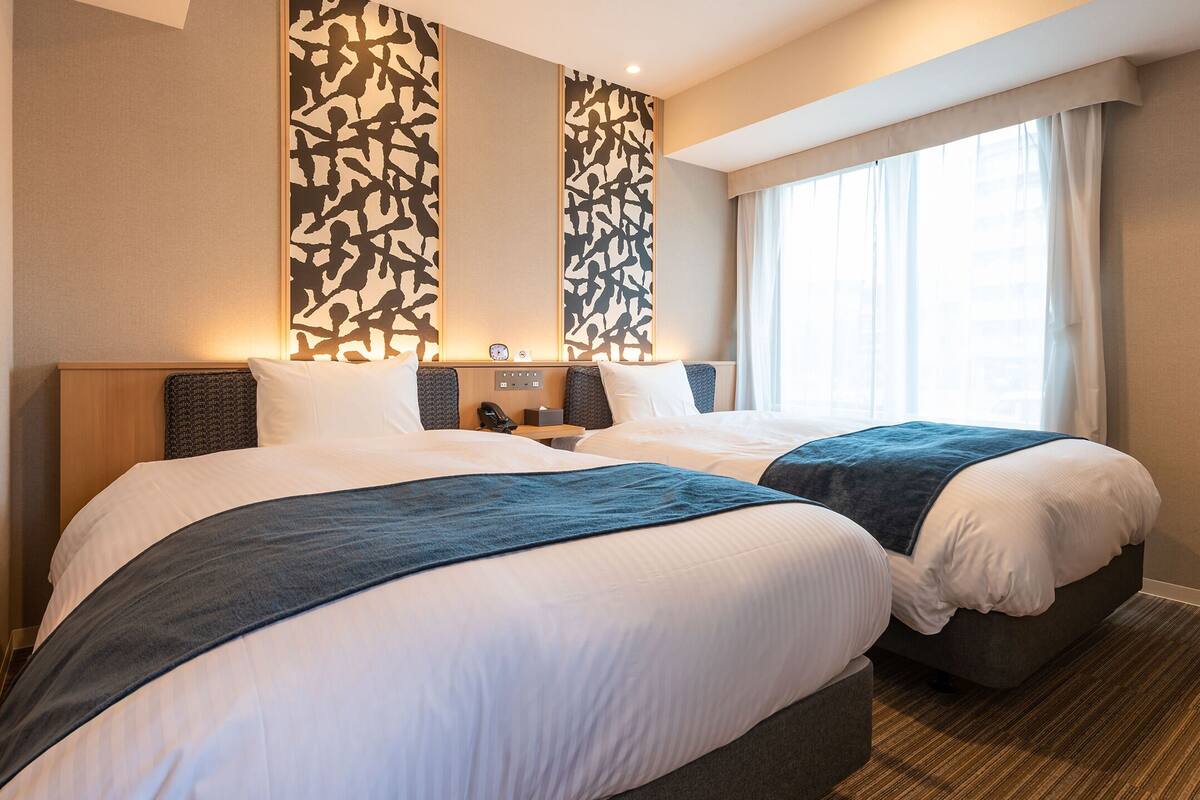 Une chambre d’hôtel avec deux lits, une table de chevet, une horloge et une fenêtre avec des rideaux.